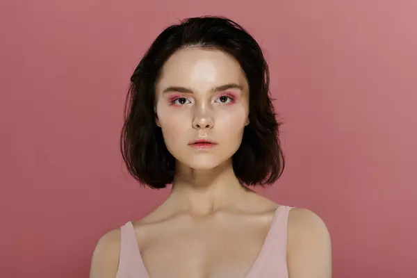 Stock image A woman with short dark hair poses against a vibrant pink background.