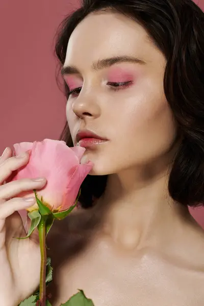 stock image A young woman with pink eyeshadow holds a pink rose to her nose.