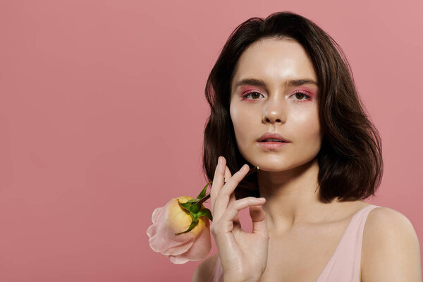 Женщина с розовой тенью для век позирует на мягком розовом фоне, держа розовую пастельную розу.