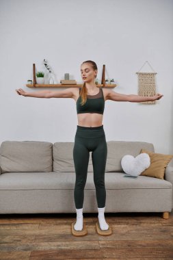 Spor elbiseli genç bir kadın oturma odasında yoga pozu veriyor..