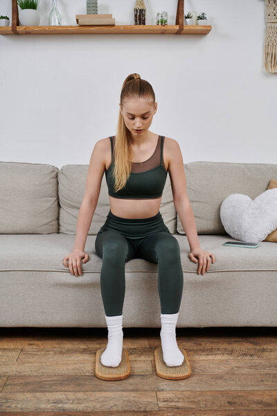 A woman in workout clothes relaxes at home, using foot massage mats.