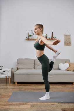 Sporcu bir kadın oturma odasındaki yoga minderine gerinir..