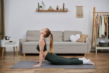 Genç bir kadın oturma odasında yoga minderine uzanır..