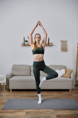 Genç bir kadın oturma odasında yoga yapıyor..