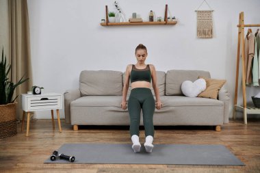 Genç bir kadın oturma odasında kanepe kullanarak egzersiz yapıyor..