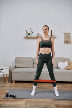 Genç bir kadın evde direniş bandı kullanarak bacak egzersizi yapıyor..