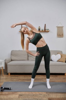 Genç bir kadın, oturma odasında yoga minderine uzanıp, rahatlatıcı bir ev egzersizi yapıyor..