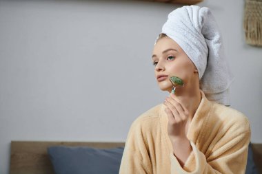 A young woman relaxes at home, using a jade roller on her face. clipart