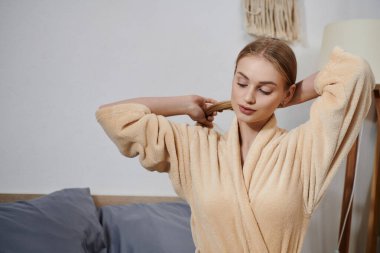 A young woman in a plush robe stands in her bedroom, a moment of quiet peace before the day begins. clipart