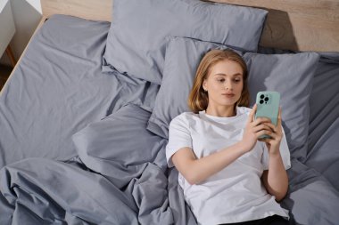Genç bir kadın yatakta uzanıyor, telefonunu karıştırıyor, huzur dolu bir anın tadını çıkarıyor..