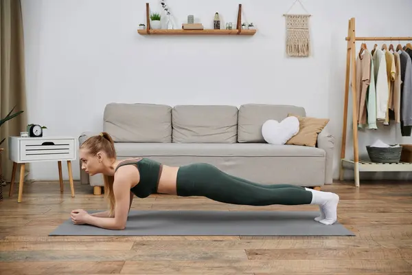 stock image A young woman in athletic wear performs a plank exercise on a yoga mat in her living room.