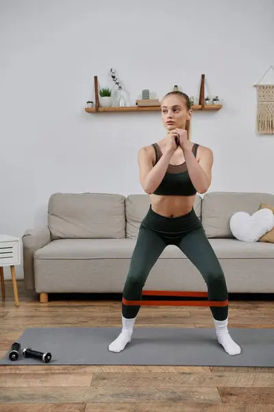 stock image A young woman exercises in her living room using a resistance band.