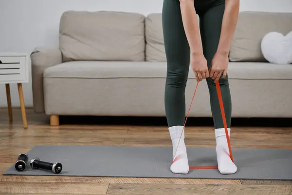 stock image A young woman doing a leg workout with a resistance band on a yoga mat in her home.