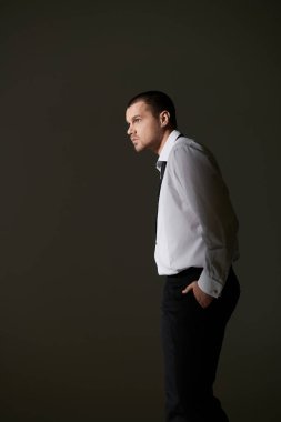 Beyaz gömlekli ve siyah pantolonlu bir adam elleri cebinde duruyor..
