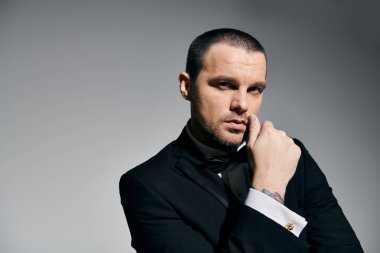 A man in a tuxedo, with a sharp haircut and thoughtful gaze, poses against a neutral backdrop. clipart