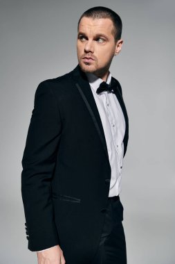 A man in a tuxedo stands against a neutral background, his gaze directed to the side. clipart