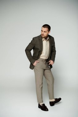 A man wearing a brown blazer and beige pants poses for a portrait in a studio setting. clipart