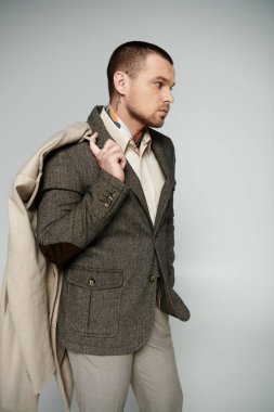 Tüvit ceketli ve açık renk pantolonlu bir adam gri bir arkaplanda rahatça poz veriyor..