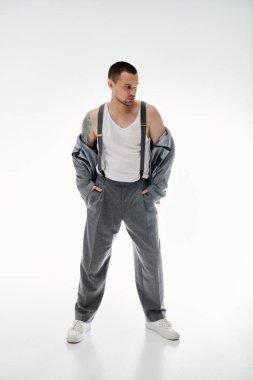 Kolsuz tişörtlü, gri pantolonlu, omuzlarının üstünde ceketi olan bir adam..