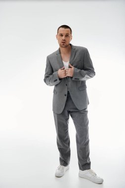 A stylish man in a grey suit stands with his jacket open, looking directly at the camera. clipart
