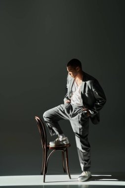Gri takım elbiseli şık bir adam bir ayağı sandalyede, diğer ayağı yerde duruyor..
