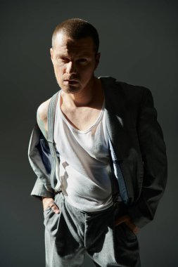 Şık bir adam stüdyo ortamında kendine güvenerek duruyor, kıyafetleri dramatik gölgeler oluşturuyor..