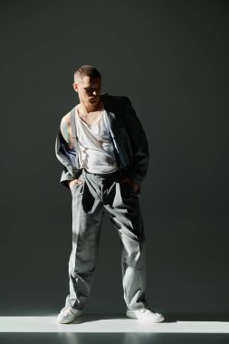 Gri pantolonlu ve ceketli bir adam stüdyoda duruyor, şık ve şık görünüyor..