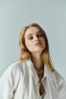 Beyaz hırkalı genç bir kadın kameraya doğru düşünceli bir şekilde bakıyor..