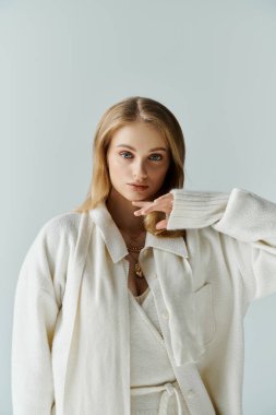 Beyaz bir elbise giymiş, eli çenesinde genç bir kadın doğrudan kameraya bakıyor..