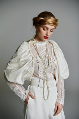 Beyaz bluz ve pantolon giymiş genç bir kadın incilerle poz veriyor..