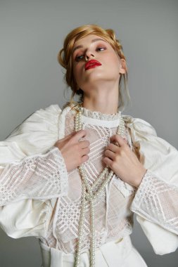 Genç bir kadın beyaz dantel bir bluz içinde inci bir kolye ile poz veriyor..