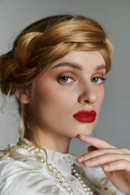 Sarı saçlı ve kırmızı dudaklı bir kadın çenesini eline dayayıp kameraya bakmıyor..