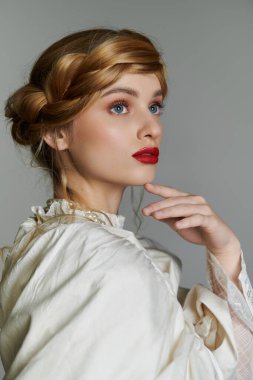 Beyaz bluzlu, inci kolyeli, saçları örgülü genç bir kadın..