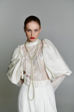 Beyaz dantelli kadın, pantolon, inci kolye, dikkatle bakıyor.