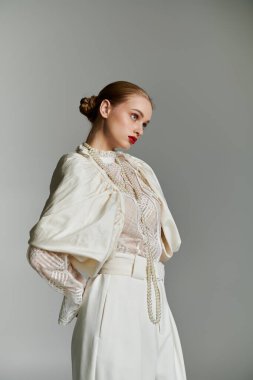 Beyaz dantelli, ceketli ve pantolonlu genç bir kadın yan tarafa bakıyor..