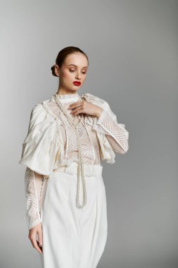 Beyaz elbiseli bir kadın gri arka planda duruyor..