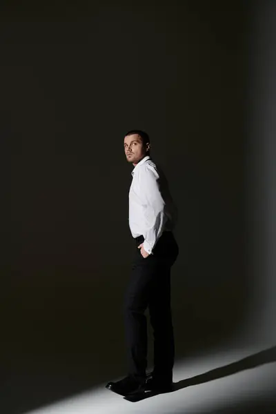 stock image A man in a white shirt and black pants stands in a spotlight, looking away from the camera.