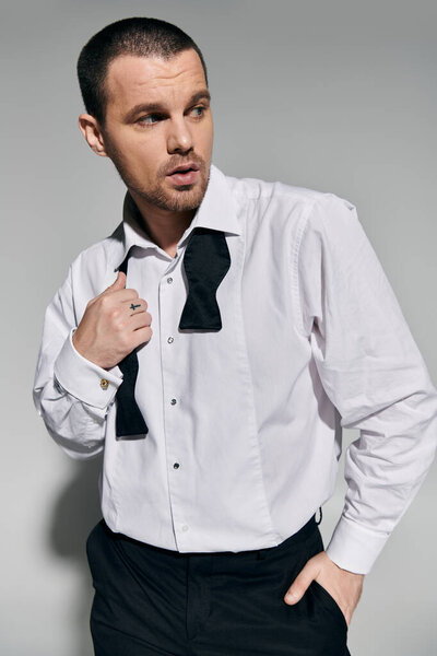 A man in a white shirt and black bow tie adjusts his attire, looking stylish and confident.