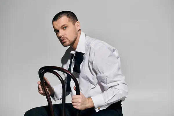 stock image A man in a white shirt and black bow tie leans back in a wooden chair, looking off to the side.