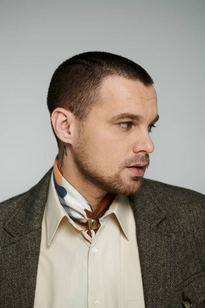 A man with a stylish haircut and a patterned scarf looks off to the side.