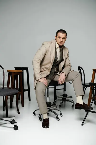 stock image A stylish man in a beige suit sits on a swivel chair surrounded by other chairs.