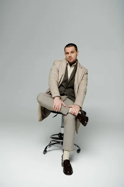 stock image A stylishly dressed man sits confidently on a stool in a studio setting.