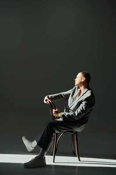 stock image A man in a grey suit sits on a chair, bathed in light.