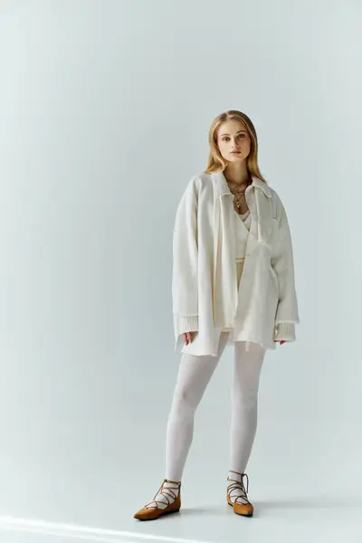 stock image A young woman stands confidently in a white outfit against a plain background.