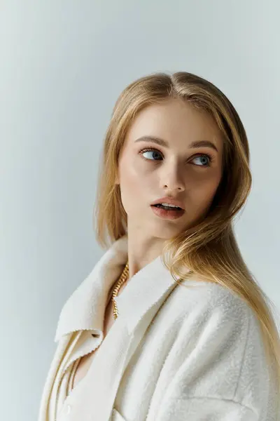 stock image A young woman with long blonde hair, dressed in a white coat, gazes off into the distance.