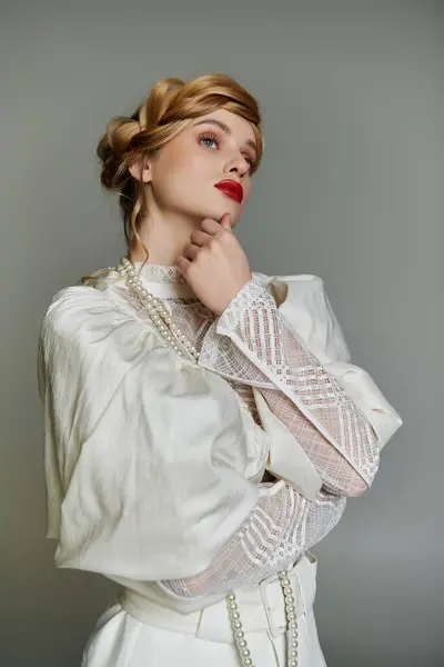 stock image A young woman in a flowing white dress and pearl necklace gazes upward, lost in thought.