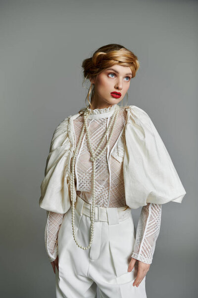 A young woman with red lipstick and a pearl necklace poses in a white lace blouse and pants.