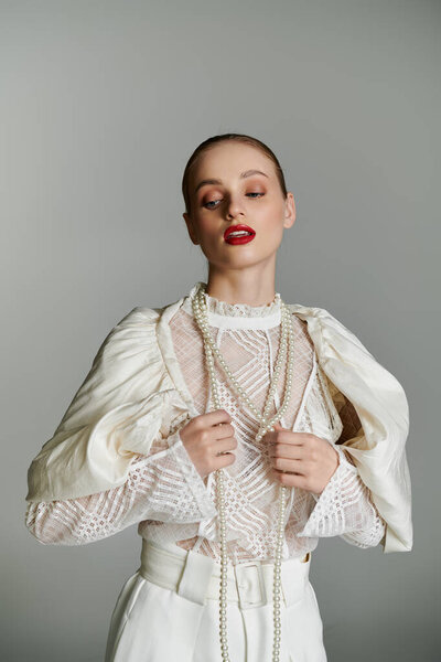 A young woman adjusts her pearl necklace, her gaze fixed on the ground.