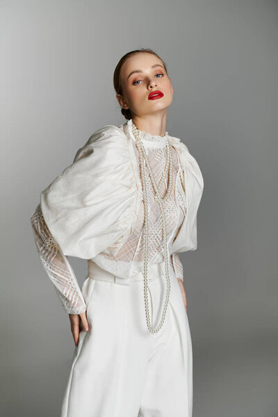 A young woman poses in a white, stylish outfit with multiple pearl necklaces.