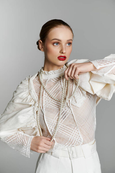 Молодая женщина в белой кружевной блузке и соответствующих брюках, украшенная жемчужным ожерельем.